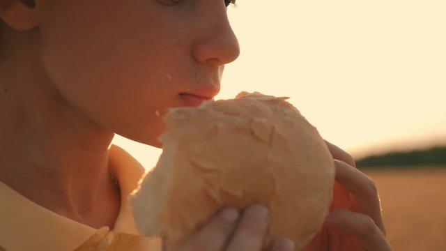 Boy farmer in a wheat field at sunset eating bread
