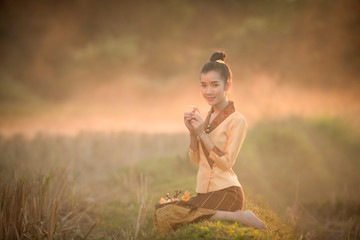Lao girl dressed in national costume sitting holding a flower at sunset in Laos