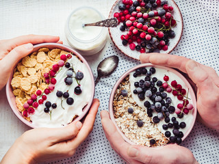 Festive and healthy breakfast for loved ones. Vintage bowls, cornflakes, granola, yogurt, fresh berries and hands of a young couple. Close-up, top view. Concept of healthy and delicious food