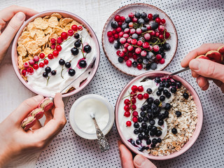 Festive and healthy breakfast for loved ones. Vintage bowls, cornflakes, granola, yogurt, fresh berries and hands of a young couple. Close-up, top view. Concept of healthy and delicious food