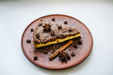 A piece of delicious chocolate cake with cream, coffee beans on a brown plate is isolated on a white background. Cinnamon, anise. happy holidays concept. Side view.
