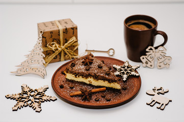 A piece of delicious chocolate cake with cream, coffee beans on a brown plate, Cup of coffee is isolated on a white background. Cinnamon, anise. Christmas decorations and gifts. Side view.