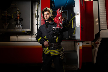 Image of man firefighter with fire cock on shoulder against background of fire truck at station