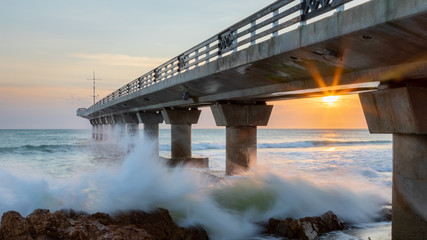 Pier in the sea at sunrise with breaking waves
