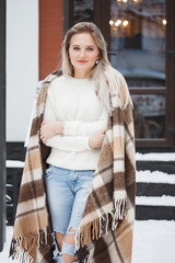 Beautiful natural young smiling shy friendly blonde woman wearing knitted sweater and plaid on a grey background.