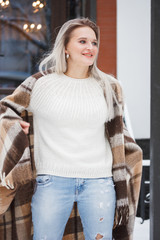 Beautiful natural young smiling shy friendly blonde woman wearing knitted sweater and plaid on a grey background.