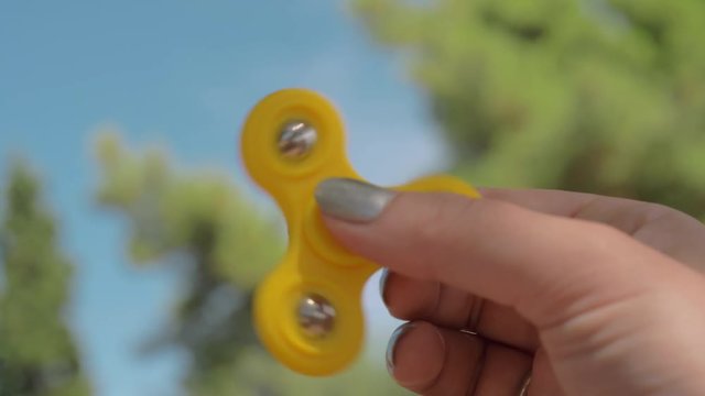 Close-up slow motion shot of woman with fidget spinner outdoor. It is spinning fast and getting slower. Antistress toy