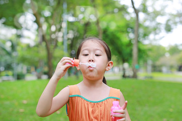 Asian little girl blowing soap bubbles in green park