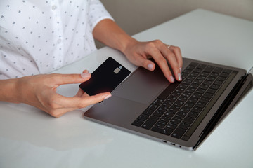 black credit card in beautiful hands of a girl in a white shirt on a white background