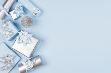 Modern soft minimalist christmas background with copy space - pastel blue and silver metallic gift boxes with shiny ribbons and bows on blue color backdrop, top view.