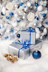 Silver gift tied with blue ribbon on white Christmas tree background