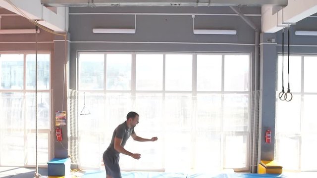 Crazy scared man with opened mouth jumping on a trampoline, fear, fobia, screaming athlete in the sport center. slow motion