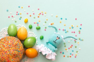 Easter celebration. Cute handmade knitted hare - a symbol of the holiday. Near her are colored eggs and Easter cake. Free space for text. Greeting card.