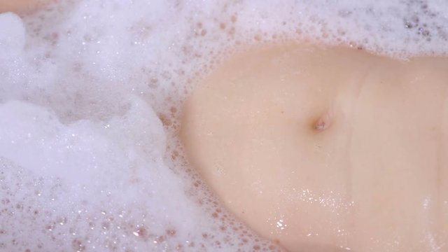 Navel on the woman's belly among the foam in the bathroom.