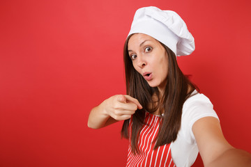 Housewife female chef cook or baker in striped apron, white t-shirt, toque chefs hat isolated on red wall background. Close up housekeeper woman doing taking selfie shot. Mock up copy space concept.