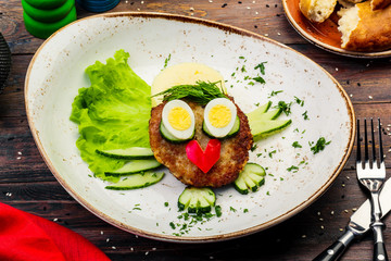 Juicy tasty meat fried cutlets with hot mashed potatoes, green lettuce leaves, on a white plate with cutlery.