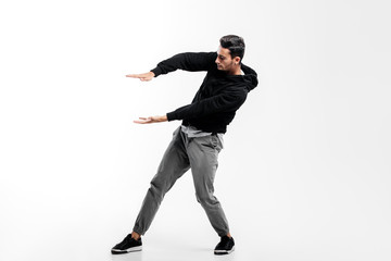 Dark-haired young man wearing a black sweatshirt and gray pants is dancing street dance. He makes stylized movements with his hands