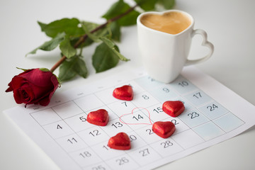 Fototapeta na wymiar valentines day and holidays concept - close up of calendar sheet with 14th february date, heart shaped chocolate candies, coffee cup and red rose