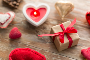 Fototapeta na wymiar christmas, valentines day and holidays concept - close up of gift box, heart shaped decorations and candle on wooden background