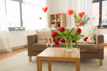 valentines day, romantic date and holidays concept - two champagne glasses and red tulip flowers on table in living room or home