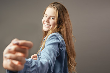 Brown-haired girl dressed in jeans shirt smiles on a gray background