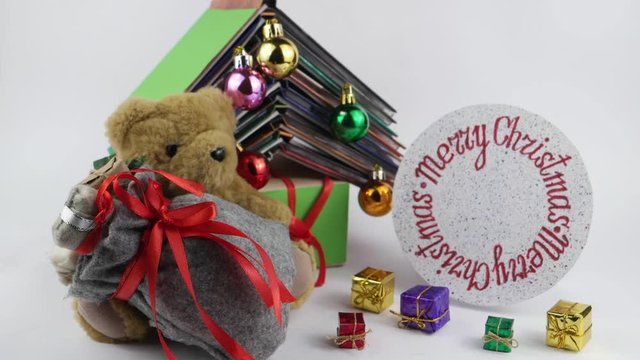A teddy bear with a bag of gifts sits on the background of the book composition in the form of a Christmas tree and rotating circle with the inscription Merry Christmas on the white background