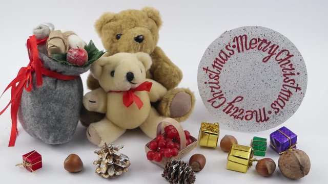 Two teddy bears with bag of gifts sit on the background of a rotating circle with the inscription Merry Christmas on the white background