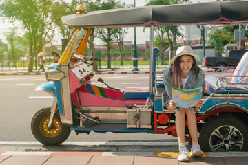  Young woman traveling people sitting on tuk tuk bangkok thailand,Cheerful woman wanderer with trendy look searching direction on location map in city centre on tuk-tuk. - obrazy, fototapety, plakaty