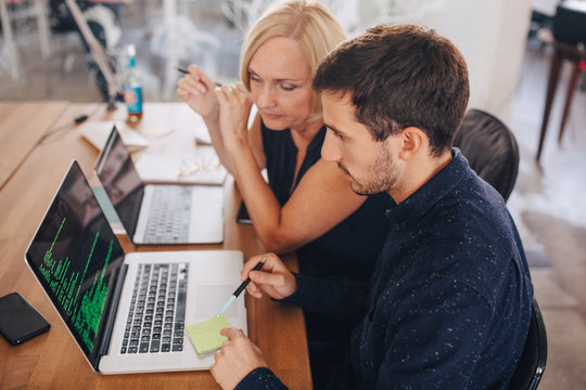 Male computer programmer explaining female colleague over laptop at desk in creative office