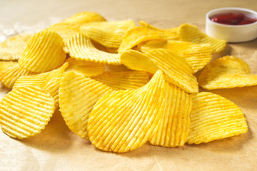 Potato chips heap and ketchup on wrapping paper, close-up