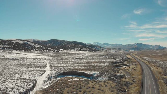 Aerial-Flying over empty two-lane road curving to distant mountains with light patches of snow on a clear winter day
