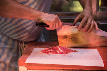 A restaurant worker is seen cutting beef meat with a butcher knife. The meat looks fresh and is ready to be sold after being cut. He is seen wearing a stripe Apron.