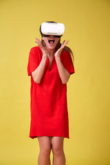 Girl in red dress and VR glasses, isolated on yellow background. Christmas or birthday emotions concept