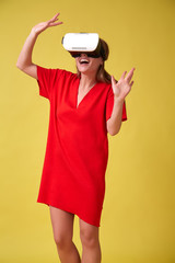 Girl in red dress and VR glasses, isolated on yellow background. Christmas or birthday emotions concept