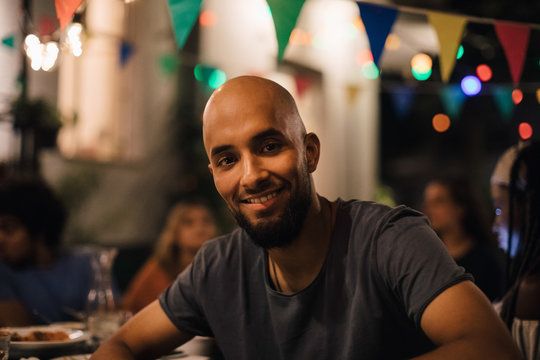 Portrait of smiling young man with shaved head sitting in backyard during dinner party
