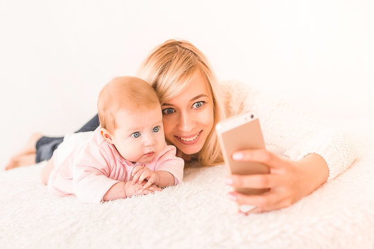 Beautiful blond mom and her daughter baby make selfie on mobile phone.