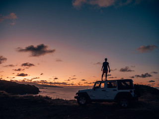 Fototapeta na wymiar a man with wanderlust standing on his car while sunset in hawaii