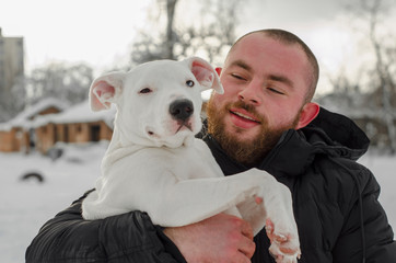 dog white pit bull with the owner, beard hipster with dark red beard while walking in the street in the winter, in a snow park, playing