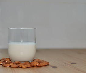 milk or almond drink in a glass with almonds and rustic wooden table background