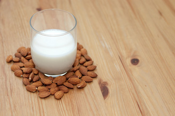 milk or almond drink in a glass with almonds and rustic wooden table background