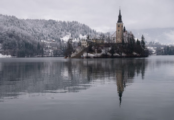 Fototapeta na wymiar Picture of Pilgrimage Church of the Assumption of Maria on an island on Lake Bled, Slovenia. Snowy capture, with moody colors