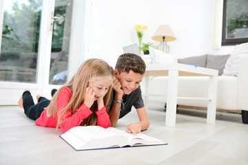 two young happy kids brother and sister together having fun at home reading encyclopedia book