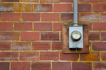 Isolated view of electrical meter mounted on weathered brick wall with open copy space to the left