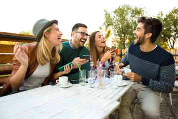 Group of four friends having fun a coffee together. Two women and two men at cafe talking laughing and enjoying their time. Using phone
