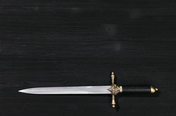 Dagger knife isolated on the black wooden background with copy space.