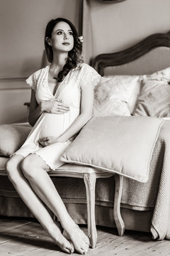 Young pregnant woman in white dress sitting in one of rooms. Image in black and white color style