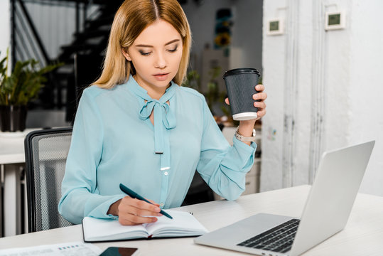 portrait of businesswoman with coffee to go at workplace with laptop and notebook