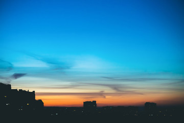 Cityscape with wonderful varicolored vivid dawn. Amazing dramatic blue sky with purple and violet clouds above dark silhouettes of city buildings. Atmospheric background of orange sunrise. Copy space.