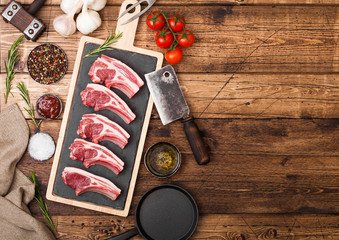 Fresh raw butchers lamb beef cutlets on chopping board with vintage meat hatchet and hammer on wooden background.Salt, pepper and oil with tomatoes and garlic and barbeque sauce. Space for text