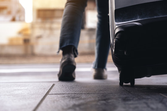 Closeup image of a woman's feet while traveling and dragging a black baggage in the outdoors